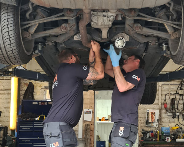 Two technicians under a vehicle installing a propshaft